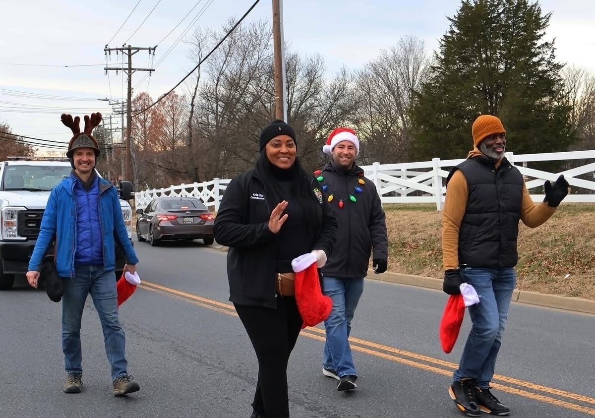 Auto-generated description: People are walking down a street, wearing festive holiday attire with some holding red stockings.