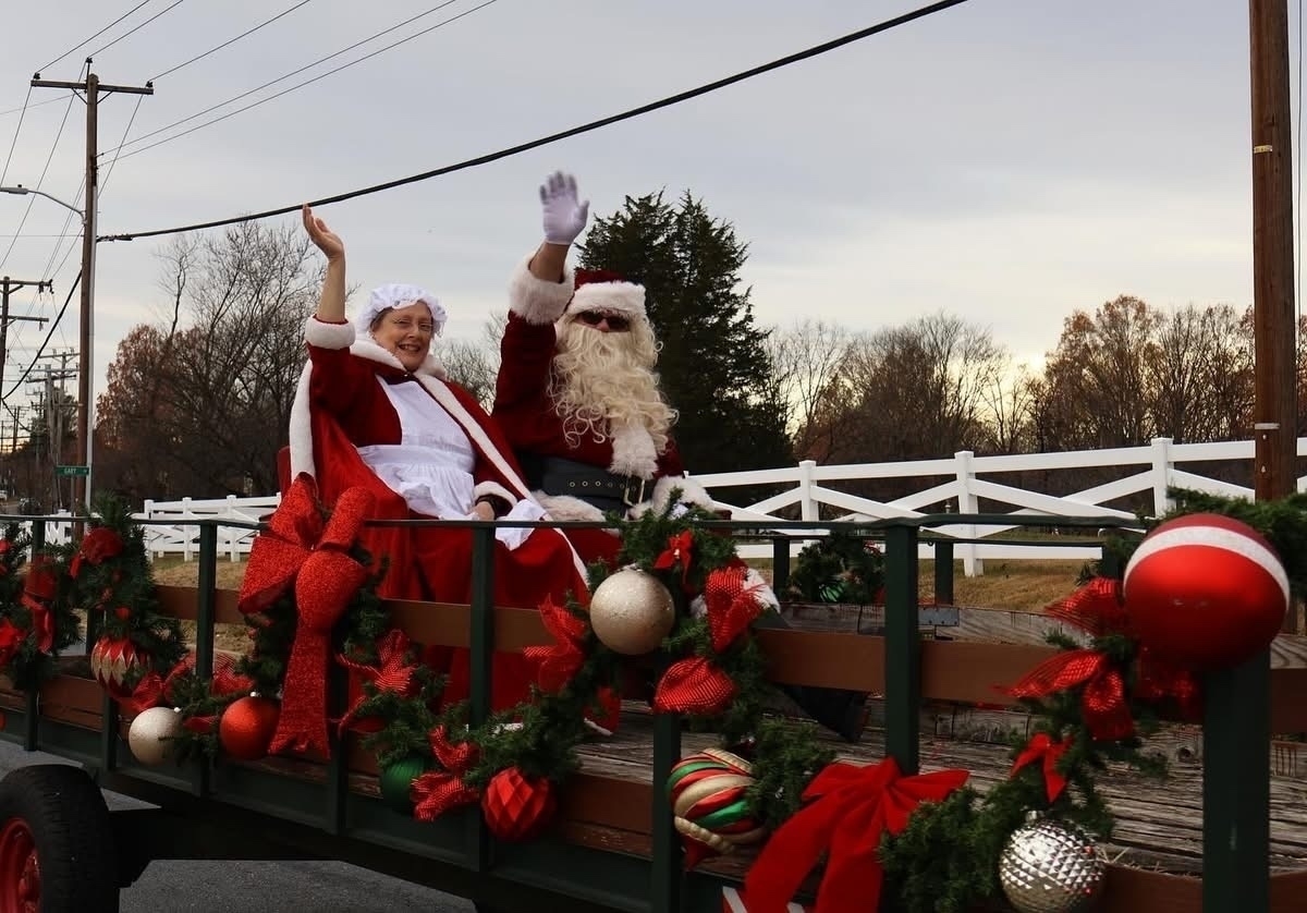 Auto-generated description: Two people dressed as Santa Claus and Mrs. Claus wave from a decorated holiday float.