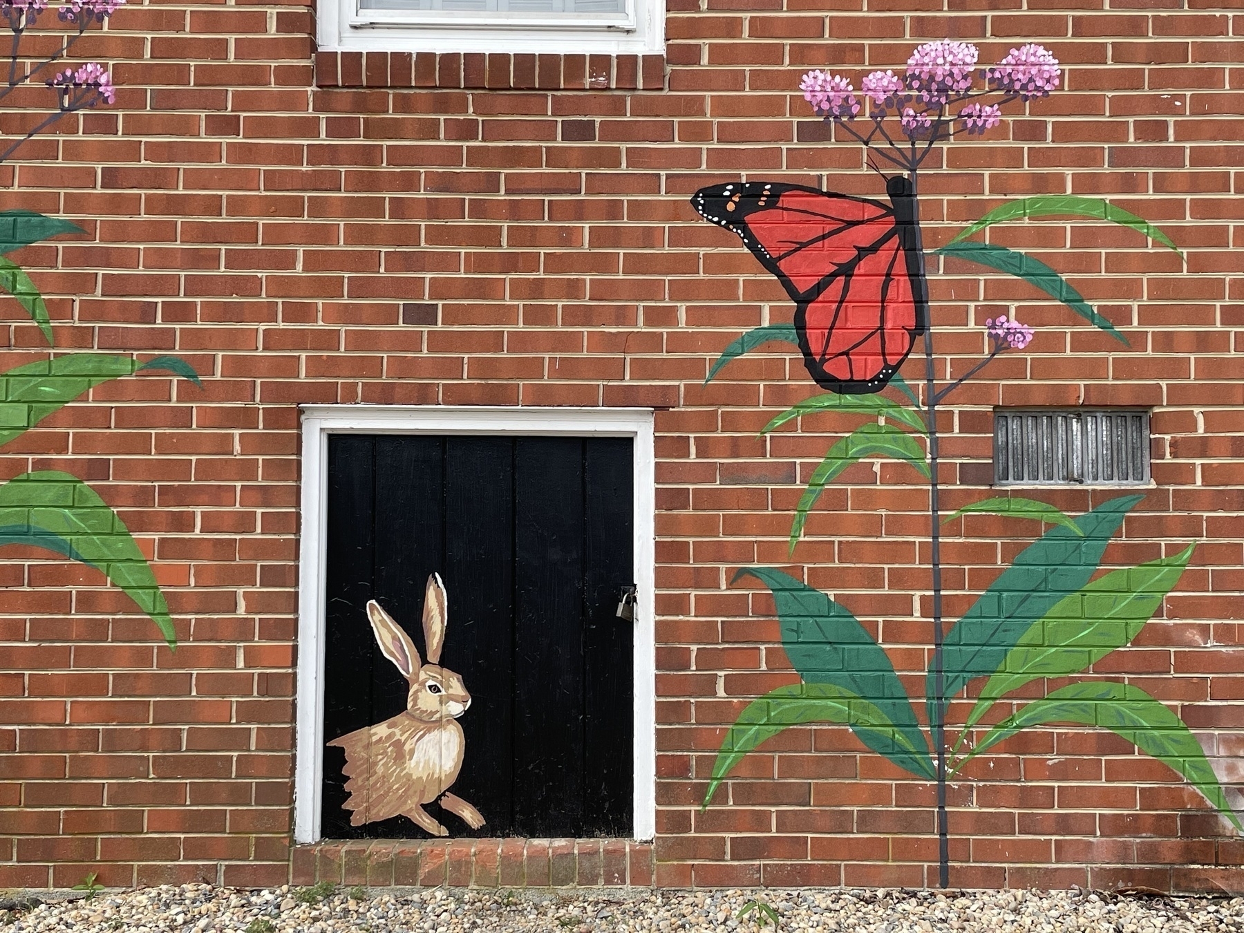 Auto-generated description: A brick wall features colorful painted murals, including a rabbit by a black door and a butterfly on flowers.