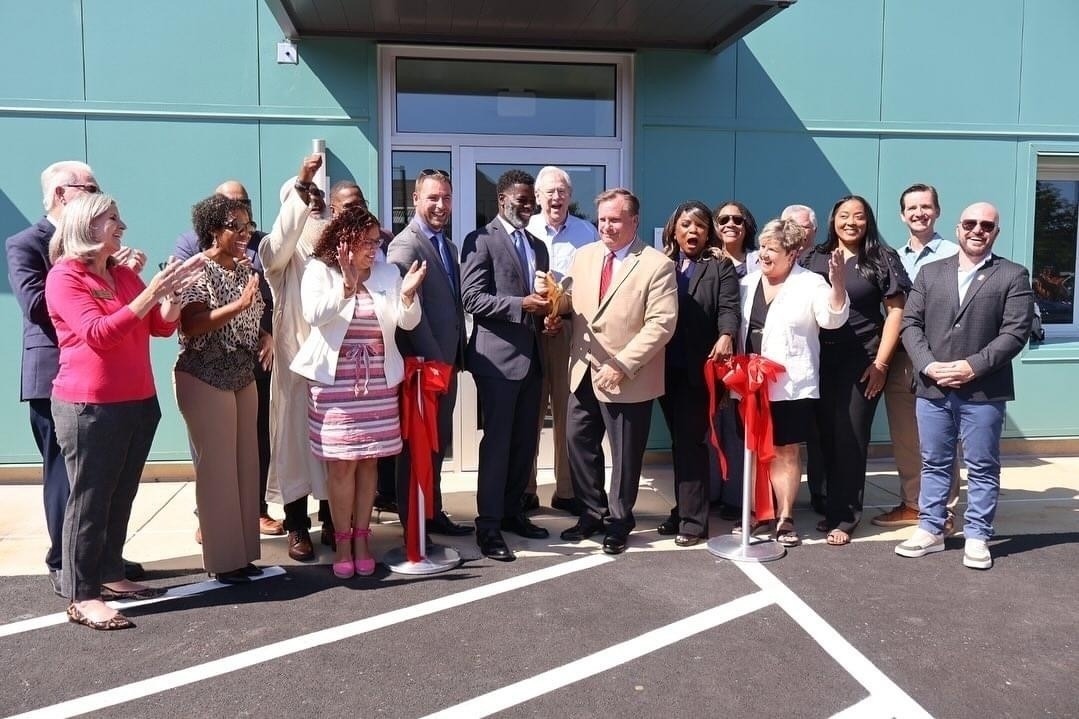 Auto-generated description: A group of people is gathered in front of a building, participating in a ribbon-cutting ceremony.