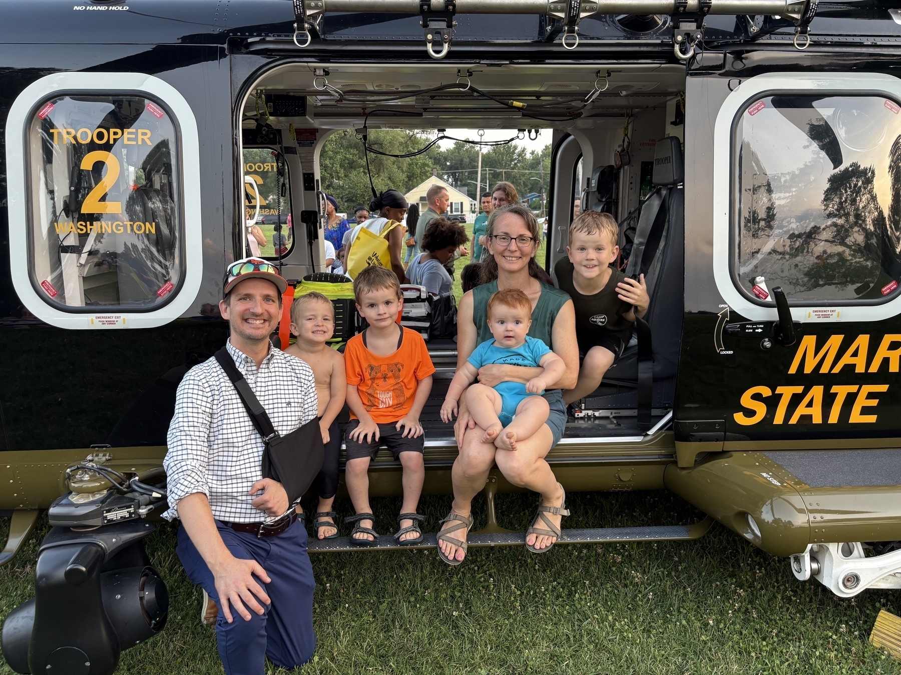 Auto-generated description: A group of people, including children and adults, are posing happily in and around a Maryland State Police helicopter.