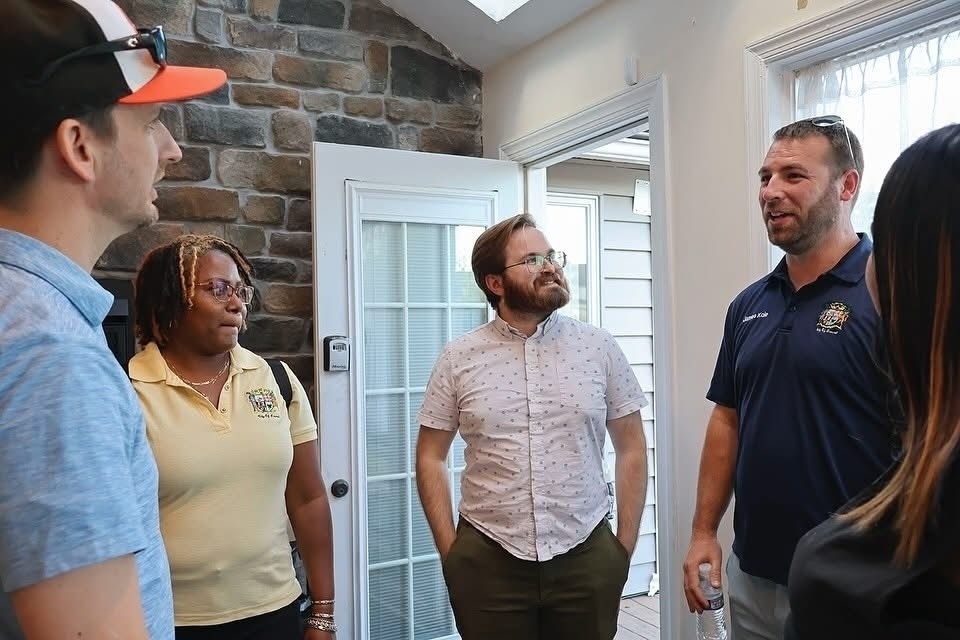 Auto-generated description: A group of people stands in a room having a conversation.