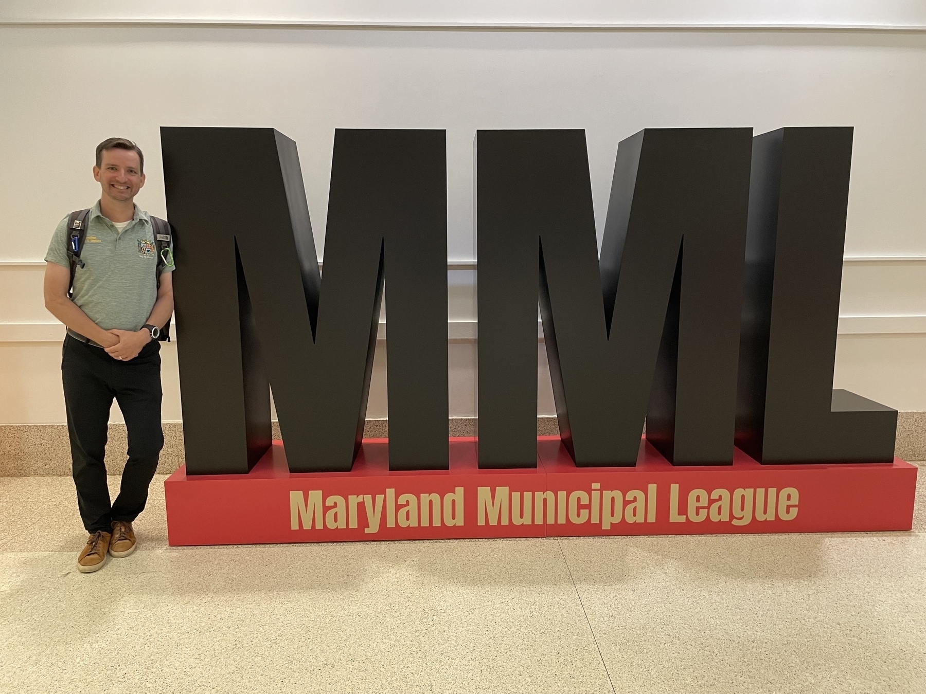 Auto-generated description: A person stands next to large letters spelling MML with Maryland Municipal League written below.