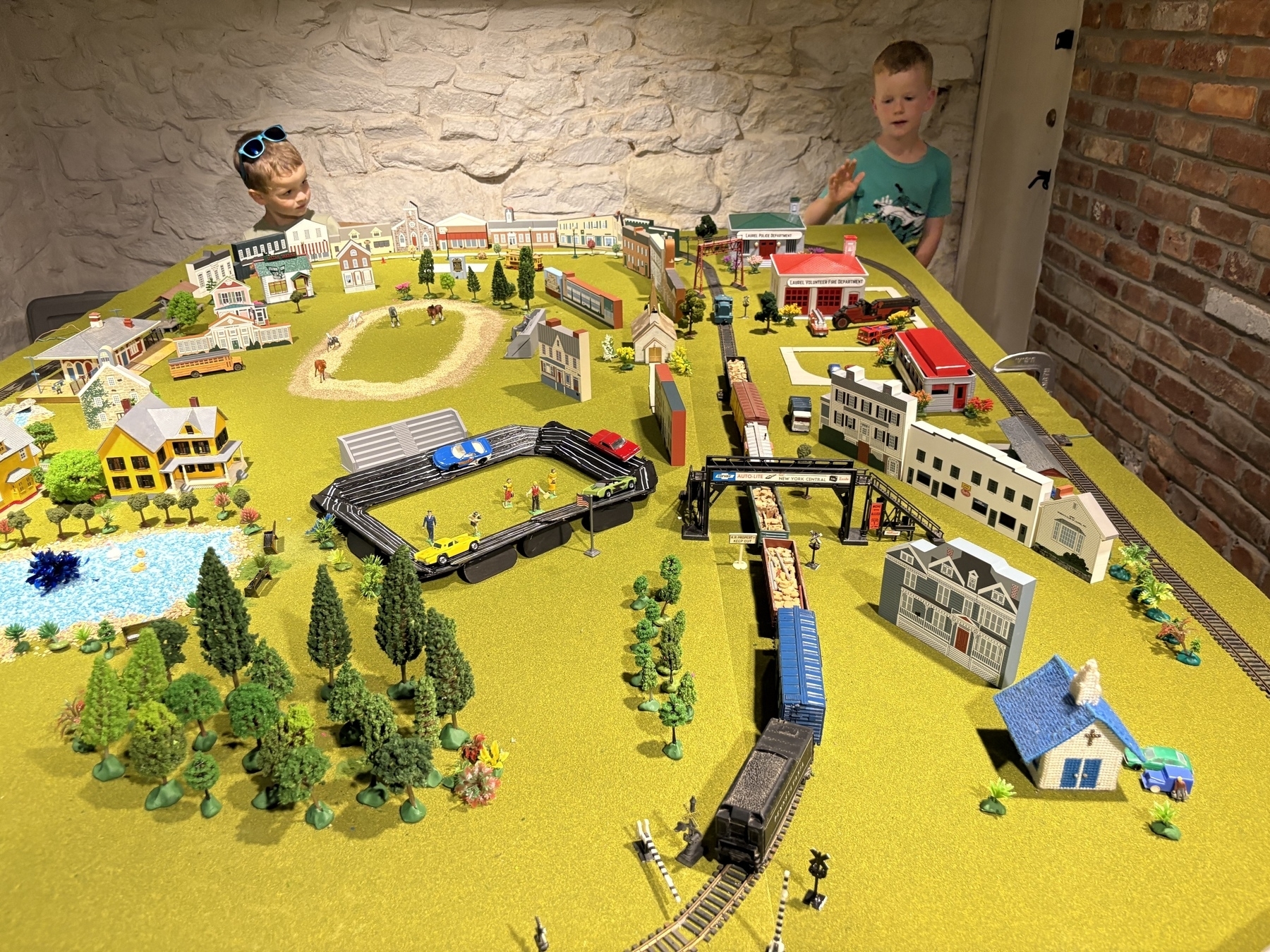 Auto-generated description: Two children are playing with a detailed model train and town setup on a large tabletop.