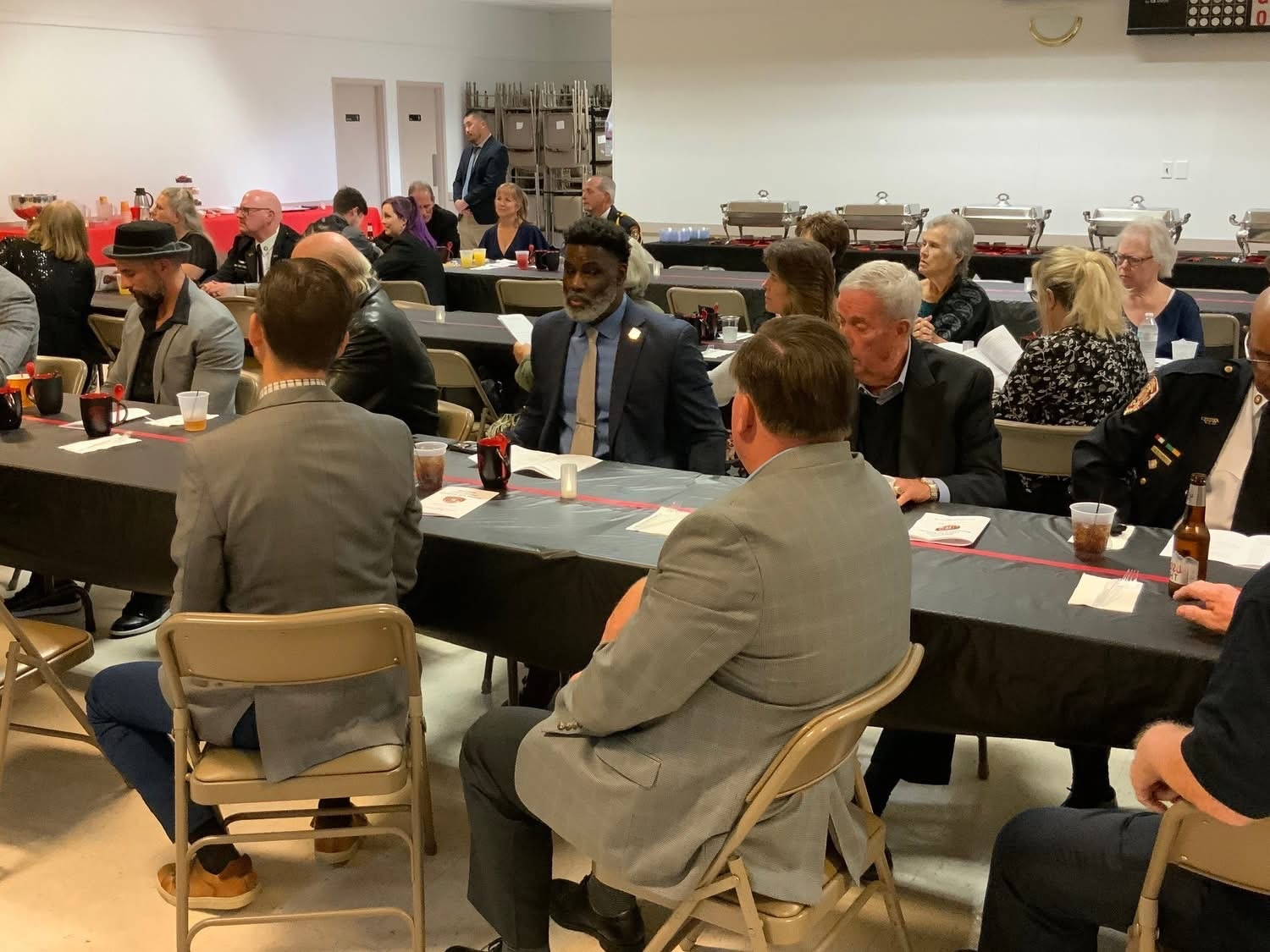 Auto-generated description: A group of people is sitting and conversing at a long table during a formal gathering or event.