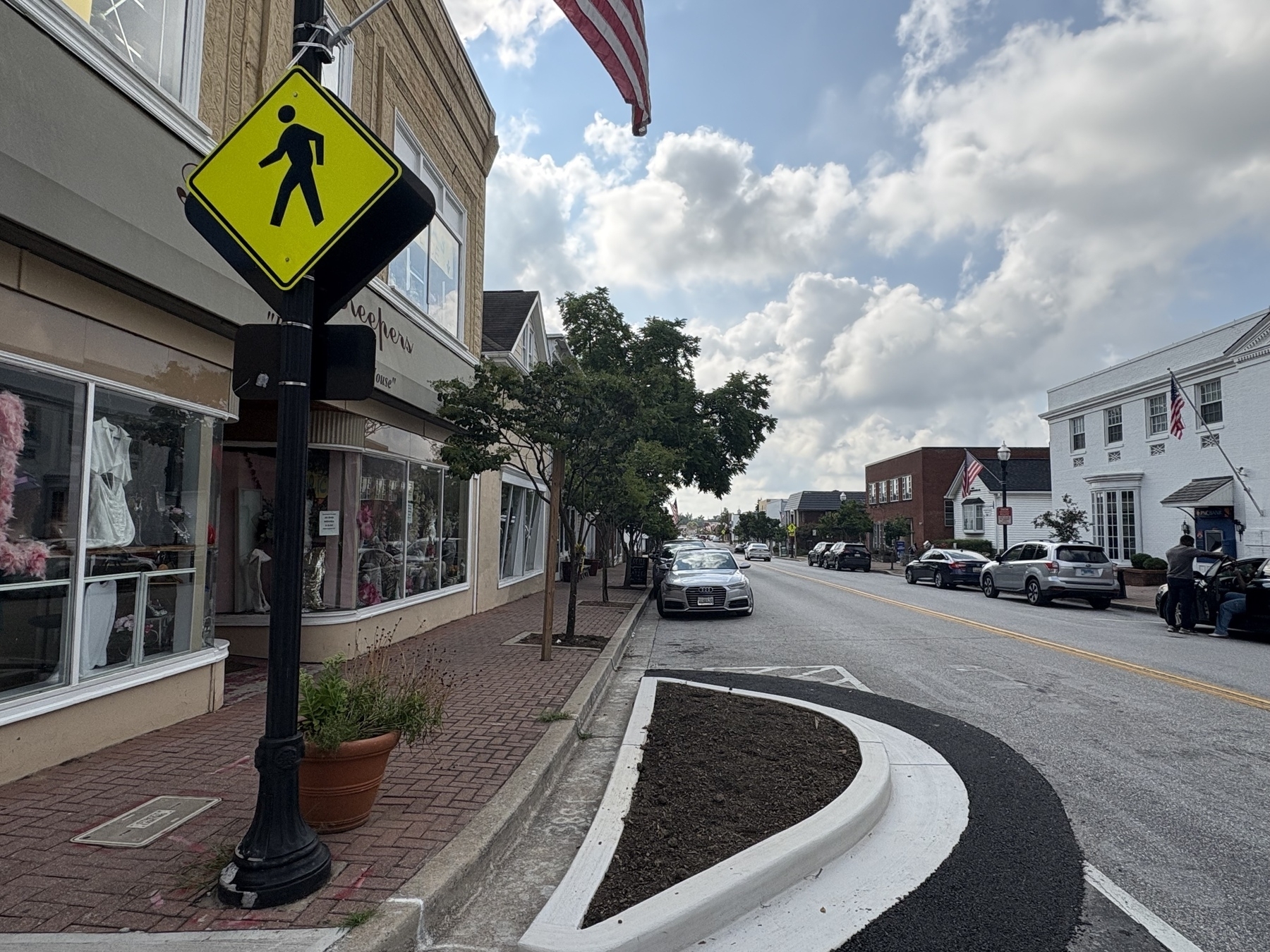 Auto-generated description: A quiet street scene features a pedestrian crossing sign, a storefront, and a parked car under a partly cloudy sky.