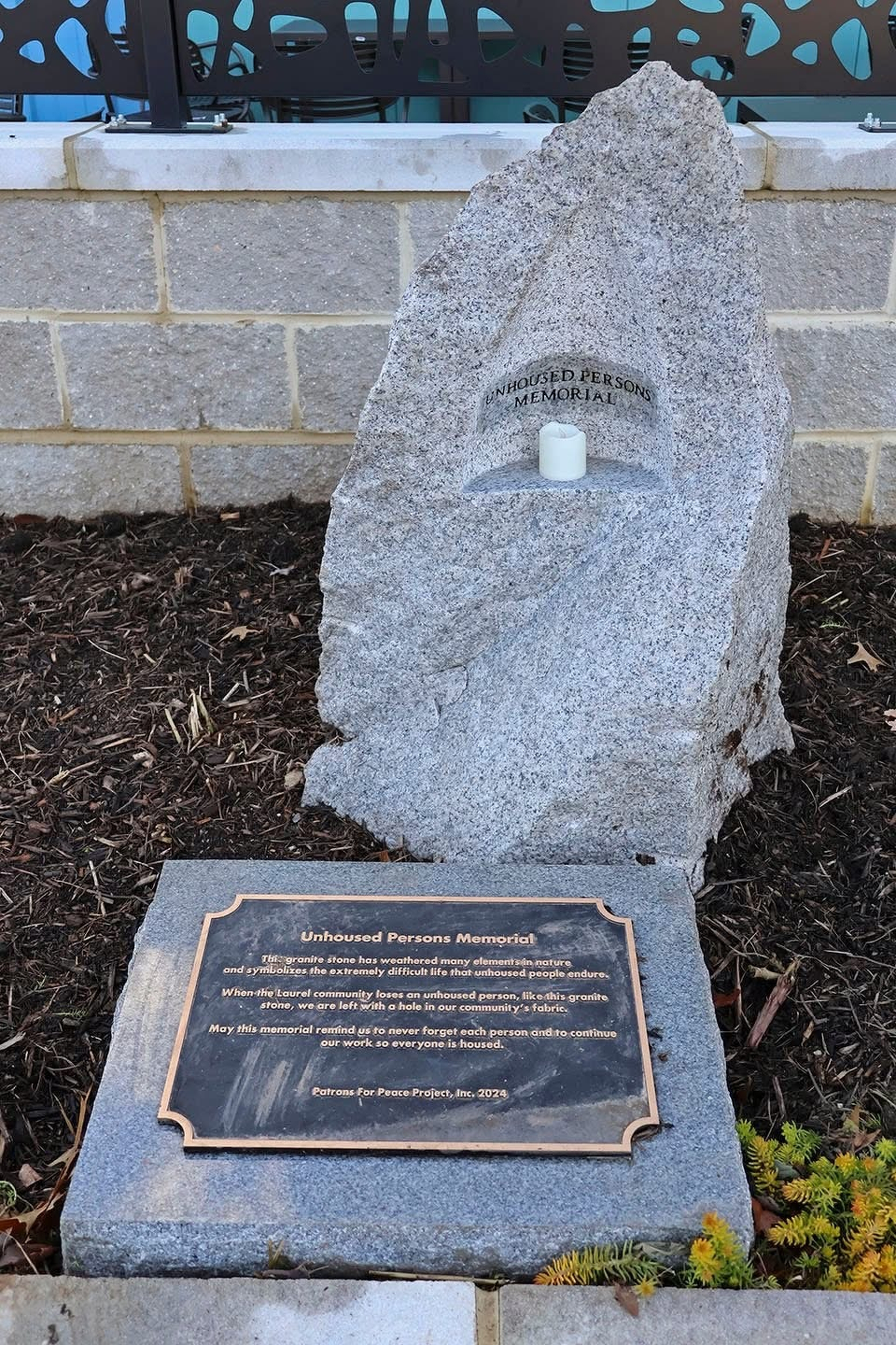 Auto-generated description: A stone memorial with a candle honors unidentified persons, accompanied by a plaque explaining its purpose.