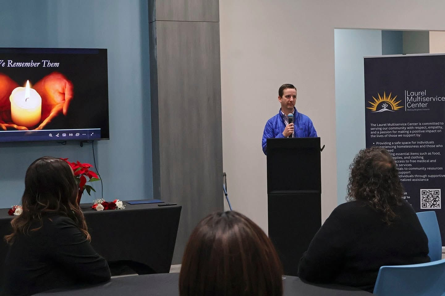 Auto-generated description: A person is speaking at a podium in a room with a screen displaying an image of a candle and hands.